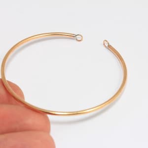 Pode incluir: Um bracelete de ouro com duas pequenas alças prateadas em cada extremidade.