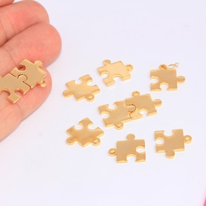 Może przedstawiać: Złote metalowe zawieszki w kształcie puzzli. Zawieszki mają kształt puzzli i mają otwór na górze do przymocowania do naszyjnika lub bransoletki.
