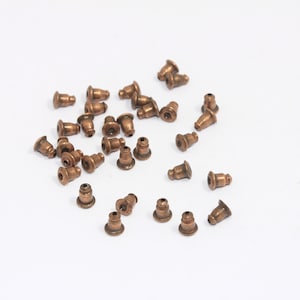 May include: A pile of small, copper-colored metal caps. The caps are about 1/2 inch in diameter and have a rounded top. They are used for finishing off jewelry projects.
