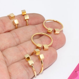 May include: Four gold rings with square accents. The rings are open and have a simple design.
