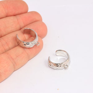 Puede incluir: Dos anillos de metal plateados con una superficie texturizada y un pequeño bucle en cada anillo.