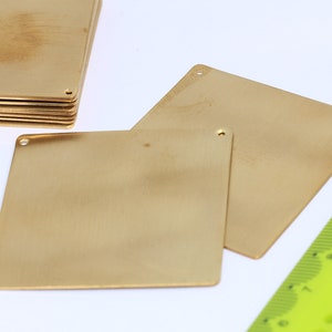 May include: Two gold-colored metal squares with rounded corners and holes in each corner. The squares are stacked on top of each other. A green ruler is in the background.