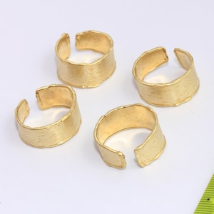 Könnte beinhalten: Vier goldfarbene Metallringe mit gehämmerter Textur. Die Ringe sind an einer Seite offen und zum Tragen am Finger gedacht.