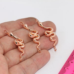May include: Three gold-toned snake charm pendants with jump rings. The charms are approximately 5 cm long and are in the shape of a snake.