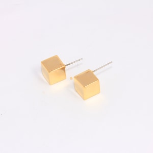 Könnte beinhalten: Ein Paar goldene Würfel-Ohrstecker. Die Ohrringe sind schlicht und elegant und eignen sich hervorragend als Geschenk für jeden Anlass.