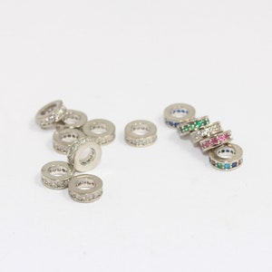 May include: A group of silver rings with clear and colored gemstones. The rings are arranged in two groups, one with clear gemstones and the other with colored gemstones.
