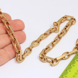 Op de afbeelding: Een gouden ketting met een getextureerd, ovaalvormig schakellinkontwerp. De ketting ligt op een wit oppervlak met een gele liniaal voor schaal.