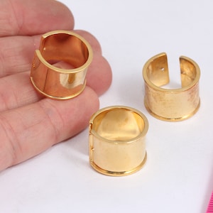 May include: Three gold-colored metal rings with a cylindrical shape. The rings are open on one side and have a smooth, polished finish.