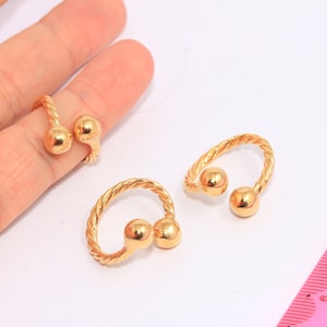 May include: Three gold-toned rings with a twisted rope design and two round balls at the top. The rings are on a white surface.