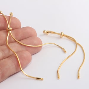 Op de afbeelding: Twee gouden kettingarmbanden met verstelbare schuifknopen. De kettingen zijn dun en hebben een delicate, licht getextureerde uitstraling.