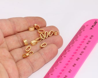 May include: A close-up of a hand holding a group of gold-colored metal oval-shaped bead caps. The bead caps are about 1 cm in length. A pink ruler with black markings is in the background.