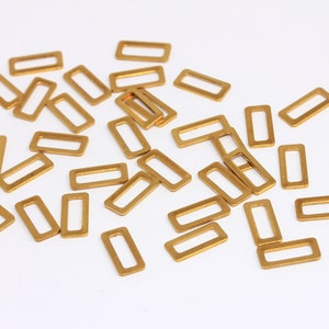 Op de afbeelding: Een stapel rechthoekige ringen van goudkleurig metaal met een kleine opening in het midden. Deze ringen worden vaak gebruikt voor het maken van sieraden en knutselen.