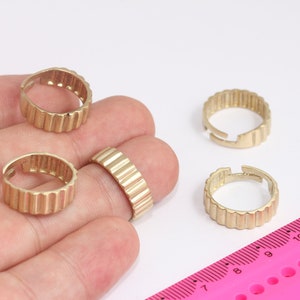 May include: Four gold-colored metal rings with a ridged design. The rings are on a hand and a pink ruler with black markings.