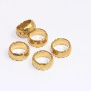 May include: Five gold-coloured metal rings with a hammered texture. The rings are stacked on top of each other.