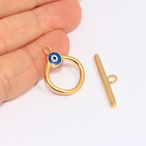 May include: Gold-tone toggle clasp with a blue evil eye charm. The clasp is made of metal and has a smooth finish. The charm is round and has a white center with a blue eye.