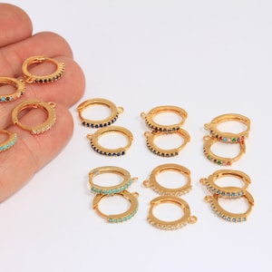 May include: A set of 10 gold hoop earrings with colorful gemstones. The earrings are arranged in two rows on a white surface.