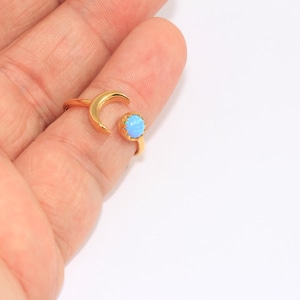 Può includere: Un anello d'oro a forma di mezzaluna con una pietra opale blu chiaro.