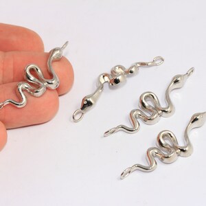 Può includere: Quattro ciondoli a forma di serpente argentati con un anello nella parte superiore per attaccarli ai gioielli. I ciondoli a forma di serpente sono in diverse posizioni, alcuni sono arrotolati e altri sono allungati.
