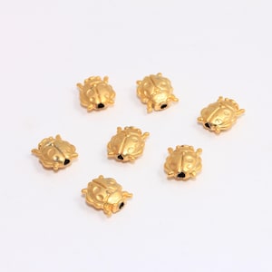 Puede incluir: Siete cuentas doradas en forma de mariquita. Las cuentas tienen un diámetro de aproximadamente 1 cm y un acabado brillante.