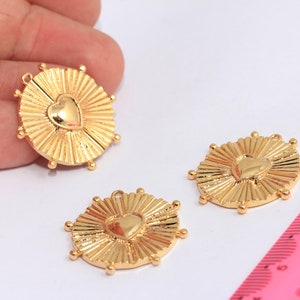 May include: Three gold-toned metal charms with a sunburst design and a heart in the center. The charms have a loop at the top for attaching to a necklace or bracelet.