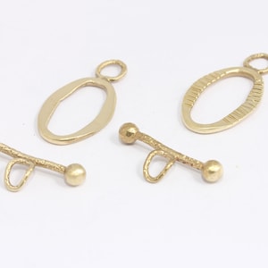 May include: Three gold-toned metal jewellery findings. Two are oval-shaped with a loop at the top. One is a bar with two round ends and a loop in the middle.