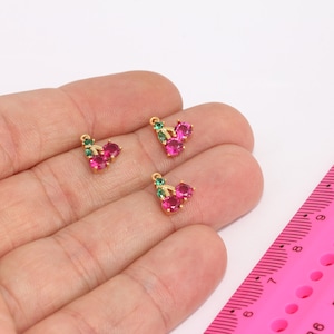 Puede incluir: Dos colgantes de cereza de tono dorado con acentos de cristal rojo y verde. Los colgantes miden aproximadamente 1 cm de largo.