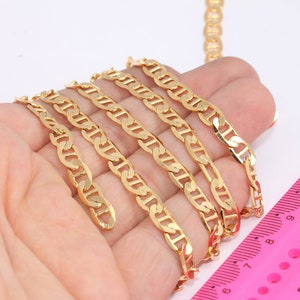 May include: Four gold-colored chains of different lengths, laid out on a hand, with a pink ruler in the background. The ruler is marked with numbers from 7 to 13 and has small circles along the edge.