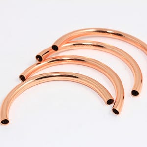May include: Four copper-colored metal hoops, each with a slightly different diameter, are stacked on top of each other. The hoops are all open and have a smooth, polished finish.