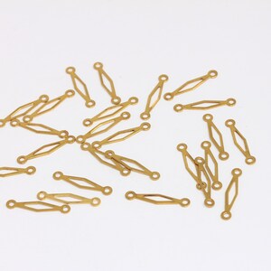Könnte beinhalten: Eine Gruppe von goldfarbenen Metallverbindungsstücken, jedes mit einer rautenförmigen Mitte und zwei runden Löchern an den Enden.