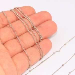 May include: Four silver chains with small beads, displayed on a hand.
