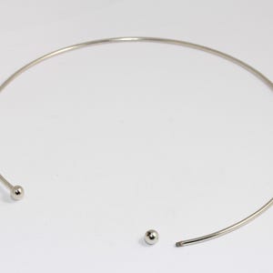 Peut inclure: Un collier ras de cou argenté avec deux petites boules argentées aux extrémités.