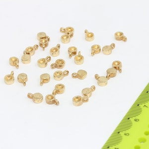 May include: A group of 20 gold-colored metal bead caps with a loop on each side. The bead caps are scattered on a white surface.