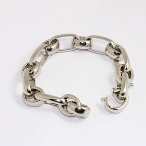 Peut inclure: Un bracelet en argent avec des maillons de chaîne et un fermoir à crochet. Le bracelet présente de grands maillons ovales reliés en boucle continue. Le fermoir est ouvert, révélant le crochet et la boucle. Sur fond blanc.