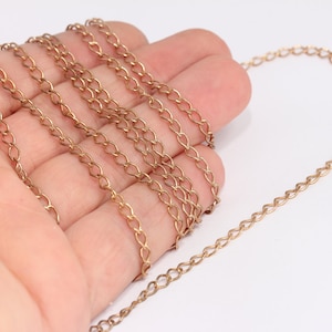 May include: A gold chain necklace with a delicate, linked design. The chain is shown coiled in a hand.