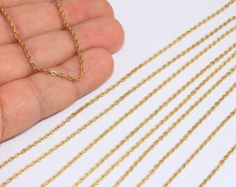May include: Close-up of multiple gold-coloured chain necklaces. The chains are thin, with small, oval-shaped links. One chain is held in a hand, while the others are arranged diagonally across a white surface.