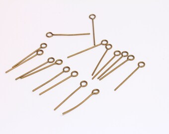 Può includere: Un gruppo di spilli per la testa dorati con un anello in cima. Gli spilli sono sparsi su una superficie bianca.