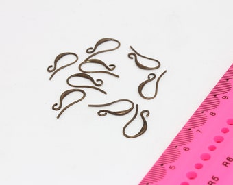 May include: A close-up of a group of 10 bronze-colored earring hooks, scattered on a white surface. A pink ruler with black markings is visible in the bottom right corner of the image.