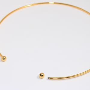 May include: A gold-toned choker necklace with two small round balls at the ends.