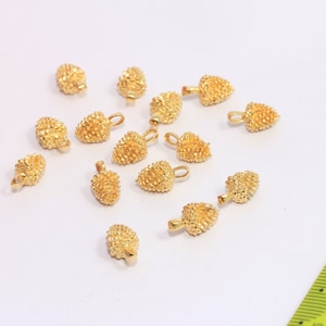 May include: A group of 14 gold-coloured metal heart-shaped charms with a textured surface. The charms have a small loop at the top for attaching to jewellery.