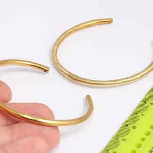 Può includere: Due braccialetti in metallo color oro, uno leggermente più grande dell'altro, sono mostrati su una superficie bianca accanto a un righello giallo. Il righello è contrassegnato da numeri da 4 a 12.