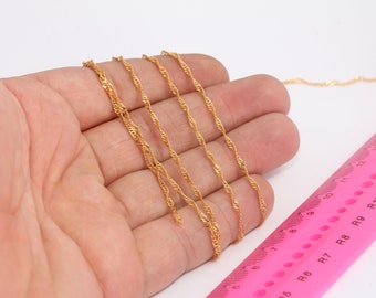 May include: Five gold chains of varying lengths laid out on a hand, with a pink ruler in the background. The ruler is marked with numbers and letters.