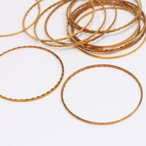 Op de afbeelding: Een set gouden metalen armbanden met een textuur. De armbanden zijn op elkaar gestapeld en in een cirkel gerangschikt.