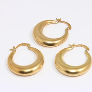 May include: Three gold hoop earrings with a smooth, rounded surface. The earrings are all the same size and shape.