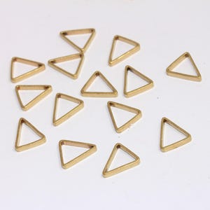 Pode incluir: Um grupo de 15 pingentes de metal de forma triangular dourada. Os pingentes são todos do mesmo tamanho e forma, e estão dispostos em um padrão aleatório sobre um fundo branco.