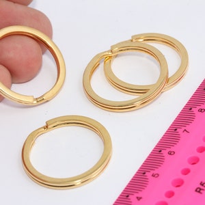 Puede incluir: Cuatro llaveros de color dorado, dos son de doble anillo y dos son de un solo anillo. Una regla rosa con marcas negras está en el fondo.