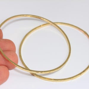 May include: Two gold bangle bracelets with a hammered finish. The bracelets are stacked on top of each other.