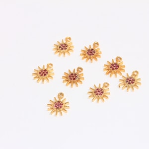 May include: Eight gold-tone sun charms with pink rhinestone accents. The charms have a loop at the top for attaching to jewelry.