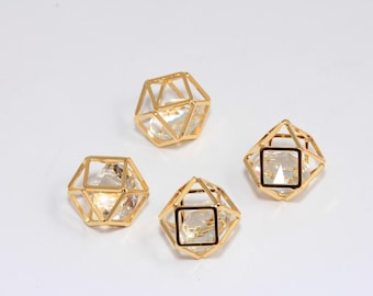 Puede incluir: Cuatro colgantes geométricos de cristal de color dorado. Cada colgante tiene un centro de cristal transparente y un marco de color dorado. Los colgantes están dispuestos sobre una superficie blanca.