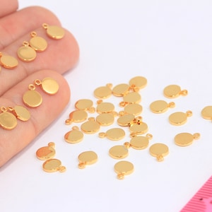Könnte beinhalten: Eine große Menge goldfarbener Metall-Kreis-Anhänger mit einem Sprungring. Die Anhänger sind auf einer weißen Oberfläche verstreut.