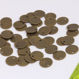以下が含まれることがあります： アンティークブラス製の丸い金属製チャームが30個積み重ねられています。各チャームには穴が開いており、直径は約2.5cmです。